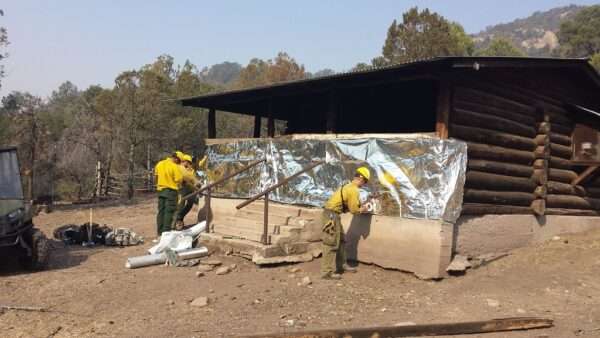 fire crew wrapping cabin in aluminized structure wrap for wildfire protection